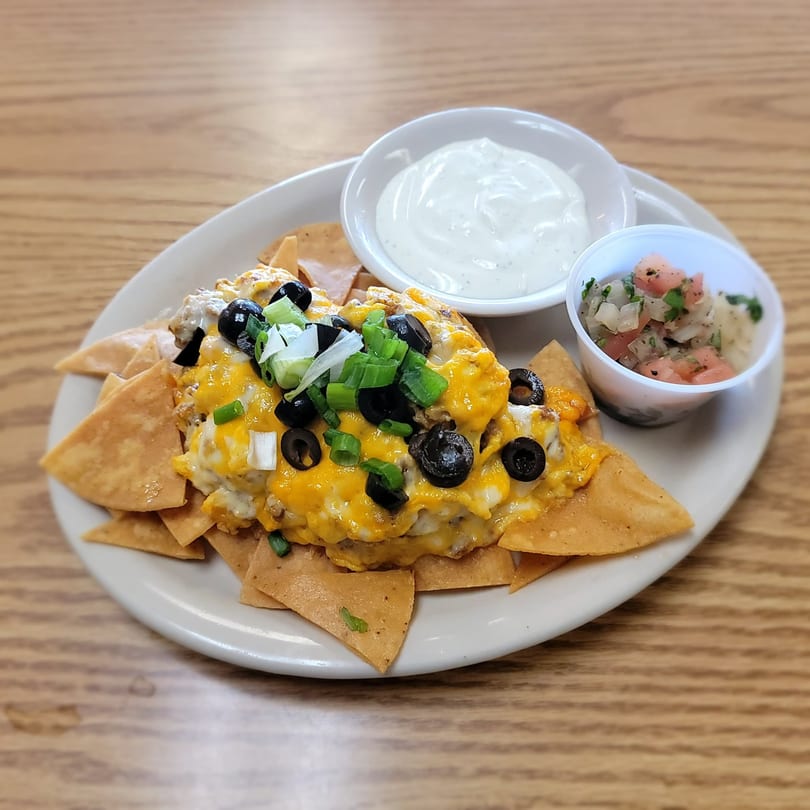A plate of nachos with melted cheese, black olives, green onions, sour cream, and salsa.