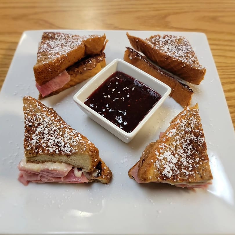 Four French toast triangles with ham and cheese, dusted with powdered sugar, and a side of jam.