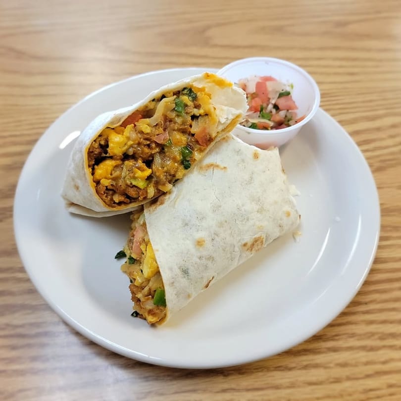 Two halves of a breakfast burrito filled with eggs, meat, and vegetables, with a side of salsa.