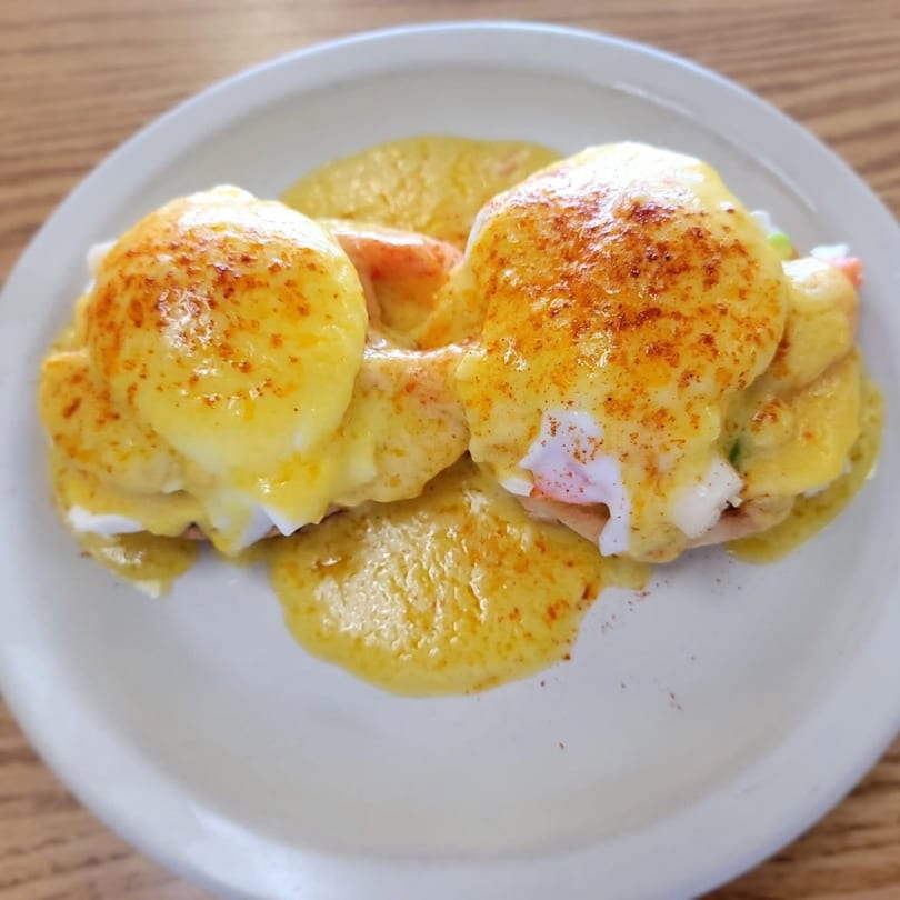 Two eggs benedict with hollandaise sauce and paprika on a white plate.